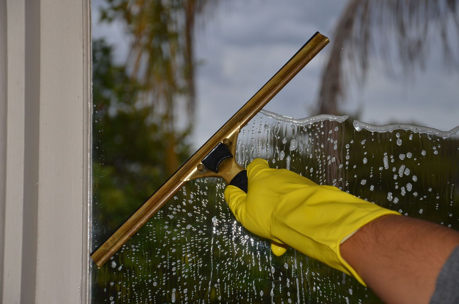 Hand mit gelbem Handschuh zieht ein Fenster außen mit dem Abzieher ab