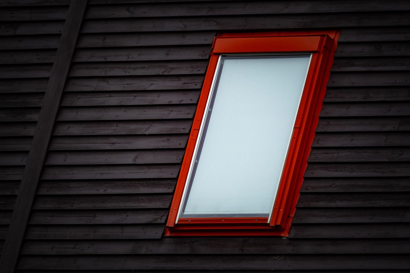 Dachfenster mit rotem Rahmen in einem dunklen Holzdach