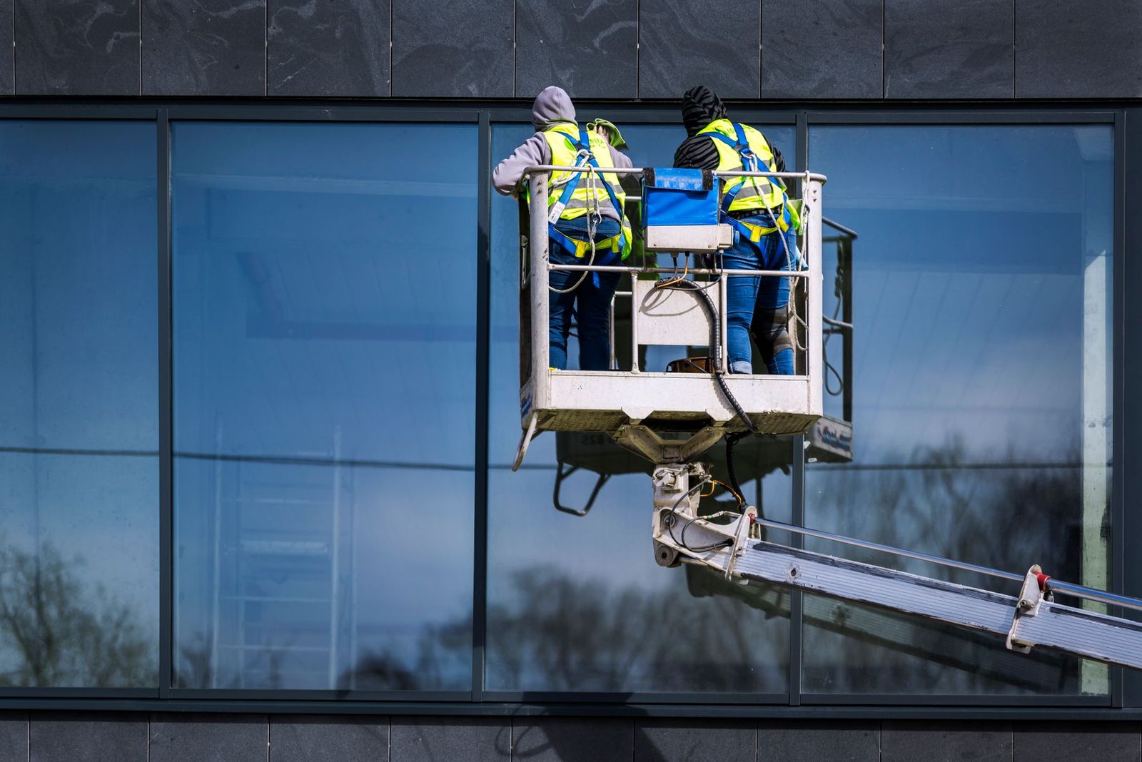 Zwei Fensterreiniger auf einer Hubarbeitsbühne an einer Glasfassade