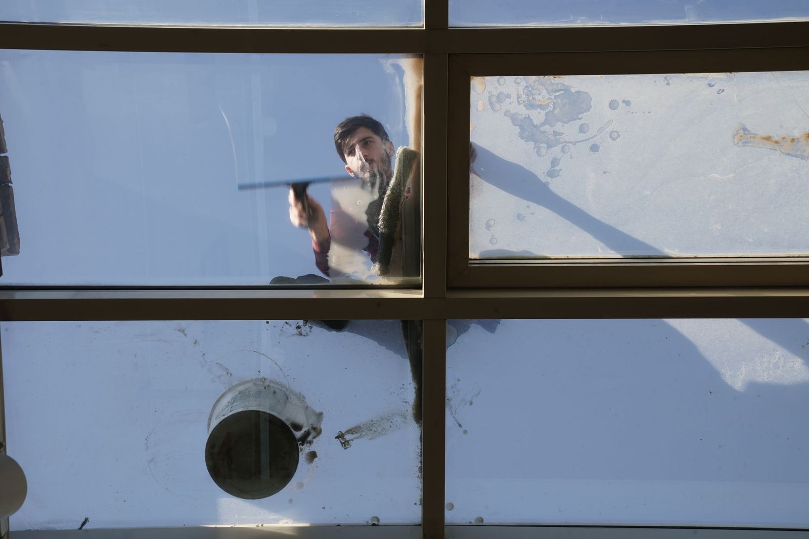 Fensterreiniger reinigt ein Glasdach von oben mit Bürste und Stange